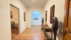 A hallway with wooden flooring, a bench, and artwork on the walls. - Charming Big Family Home in Bankstown (Bankstown)
