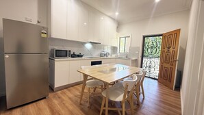 A modern kitchen with white cabinets, a stainless steel refrigerator, a microwave, and a wooden dining table with chairs. - Charming Big Family Home in Bankstown (Bankstown)
