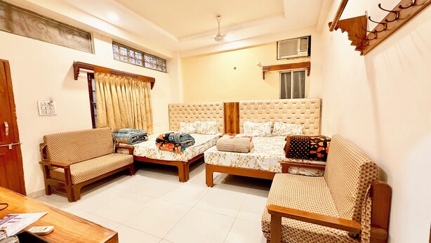 A hotel room with two single beds, a sofa, a small table, and a ceiling fan. - Hotel P & L near Mahakaleshwar Temple  (Ujjain)
