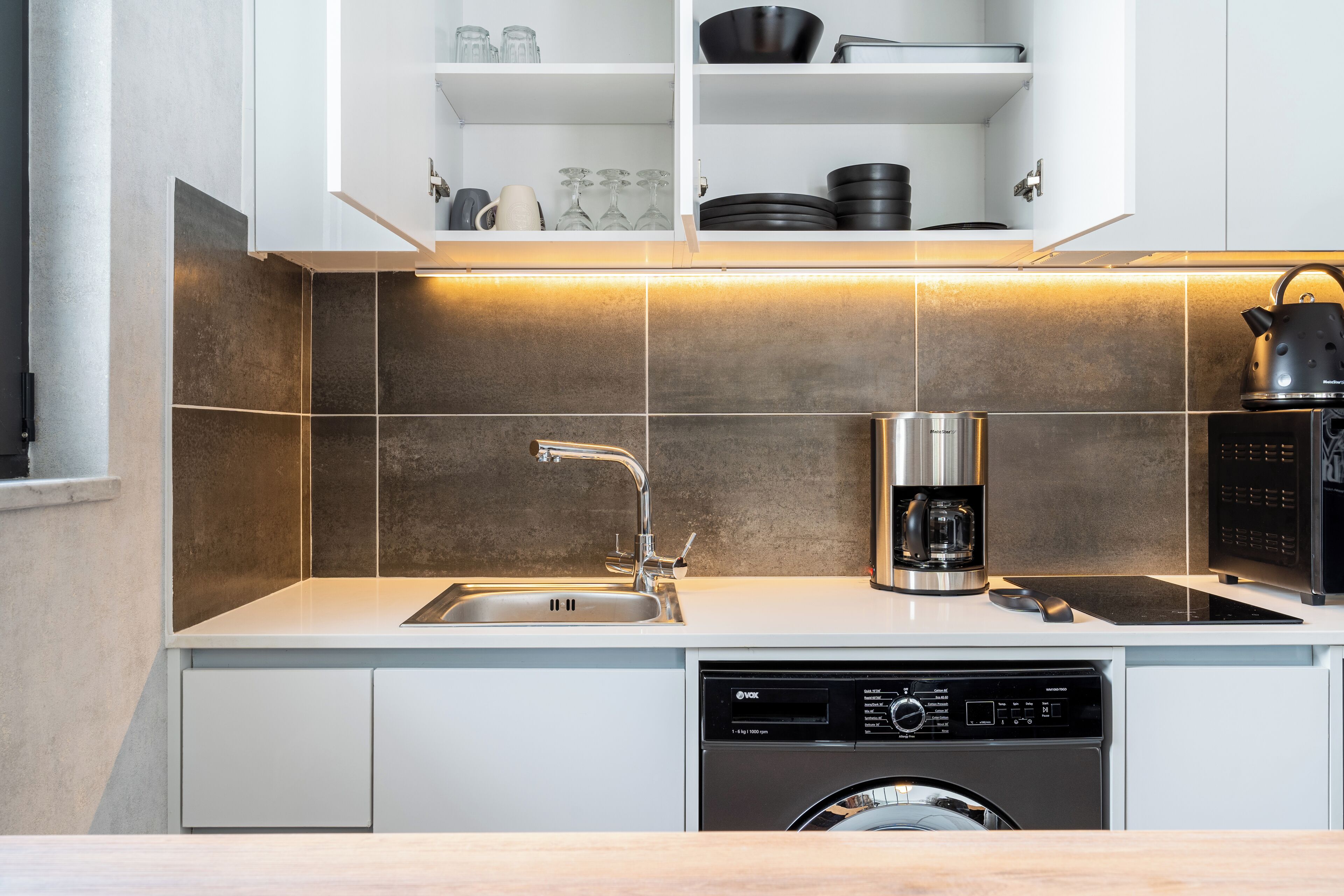 A modern kitchen with a dishwasher, coffee maker, and kettle.
