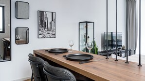 Un espace de restauration moderne avec une table en bois, des chaises noires et un tableau représentant un paysage urbain.