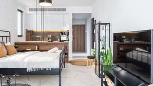 Une chambre moderne avec un lit, une table de chevet et un téléviseur. Il y a également un coin cuisine équipé d’une cuisinière, d’un évier et de placards.