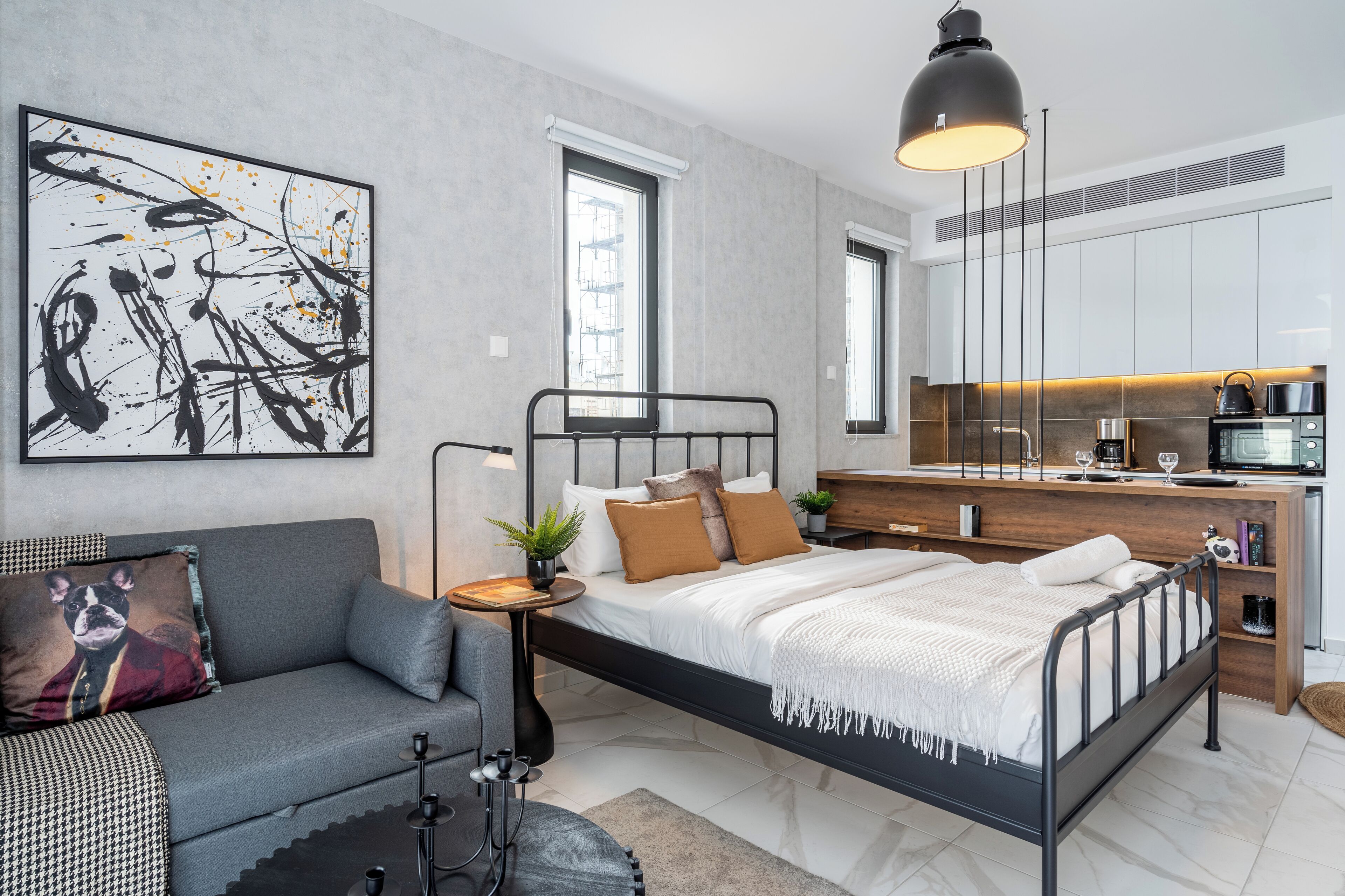 Un dormitorio moderno con estructura de cama metálica negra, sofá gris y un cuadro abstracto grande en la pared.