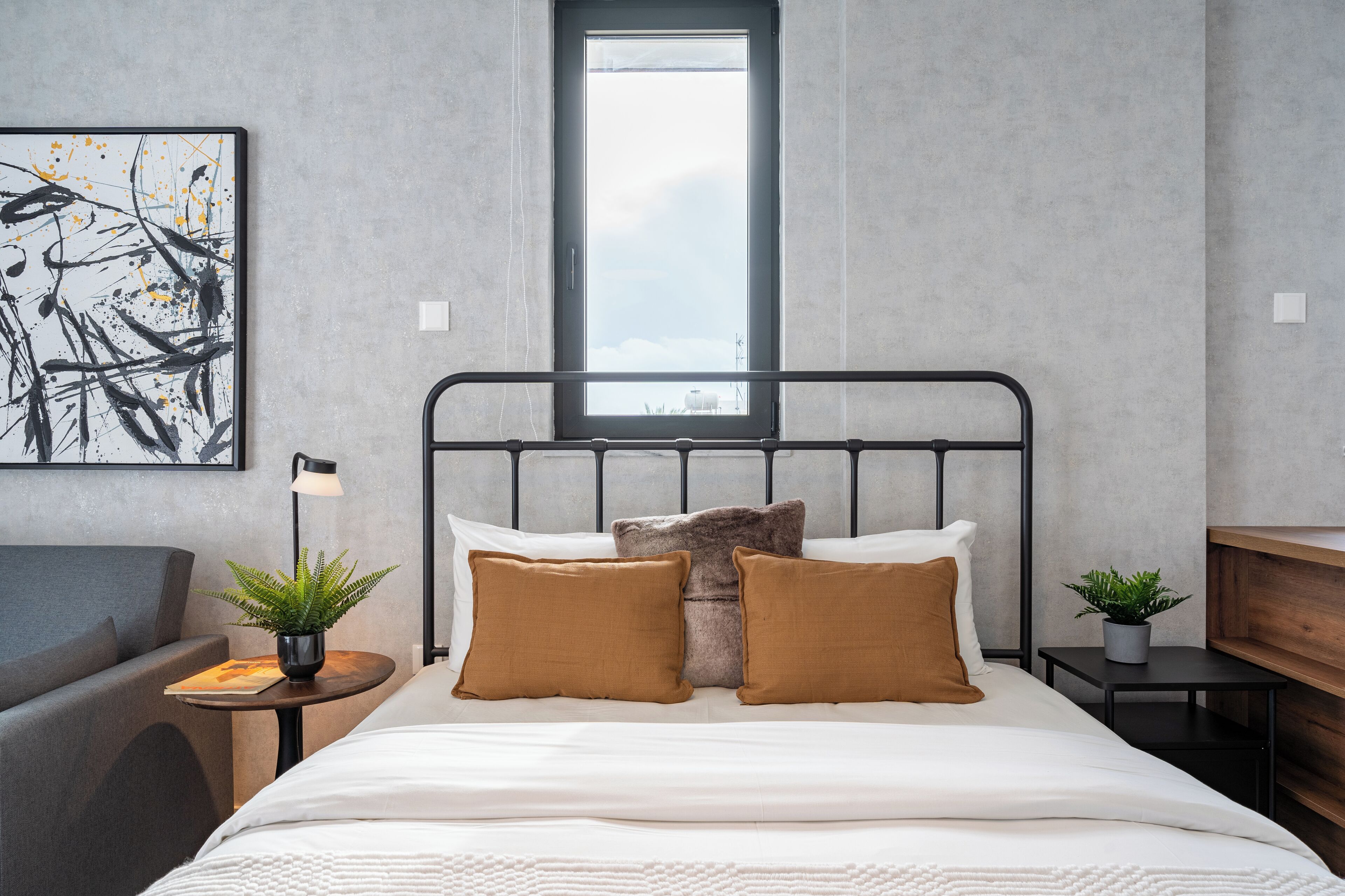 Una habitación de hotel moderna con cama, mesita de noche, lámpara y ventana con vista a la ciudad.