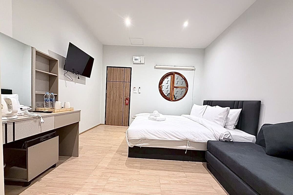 Una habitación de hotel moderna con una cama, un escritorio con computadora, un televisor de pantalla plana, un espejo redondo y un armario de madera.