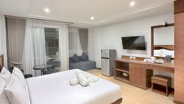 Una habitación de hotel moderna con una cama grande, un escritorio, un televisor y una pequeña kitchenette.