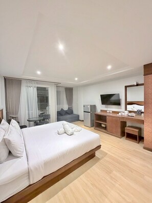 A modern hotel room with a large bed, a desk, a television, and a small kitchenette. - One Houses (Patong)