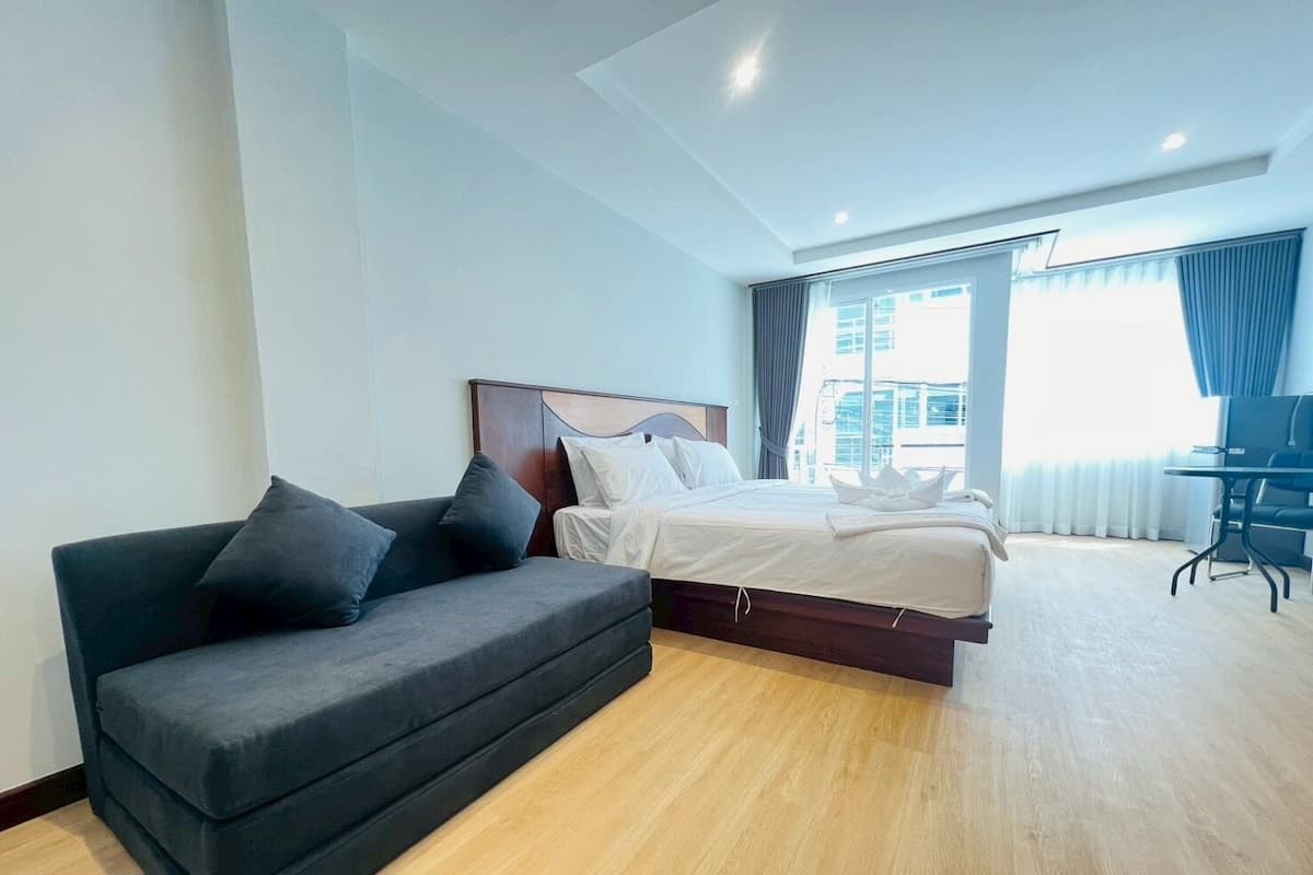 Una habitación de hotel moderna con una cama, un sofá de color oscuro y un escritorio.