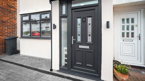 Una puerta negra con un panel de vidrio, una puerta blanca con diseño de cuadrícula y una planta en maceta con flores amarillas.