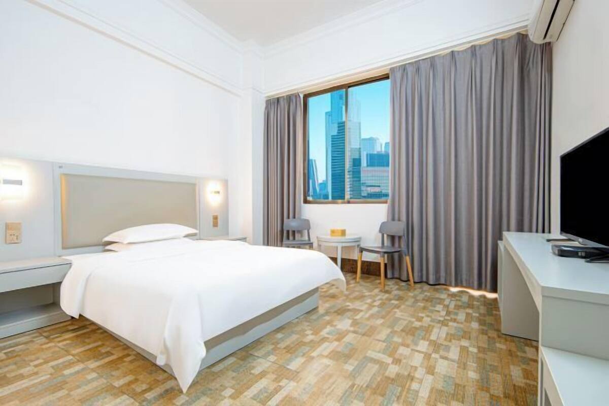 A hotel room with a bed, a desk, a chair, a small table, and a TV.