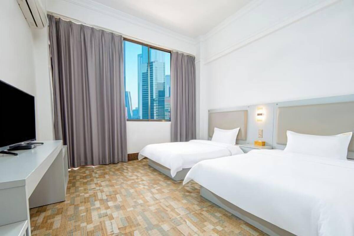 A hotel room with two beds, a TV, a desk, and a window with curtains.