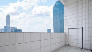 Een terras op het dak met uitzicht op stadsgebouwen, een betegelde vloer en een metalen constructie.