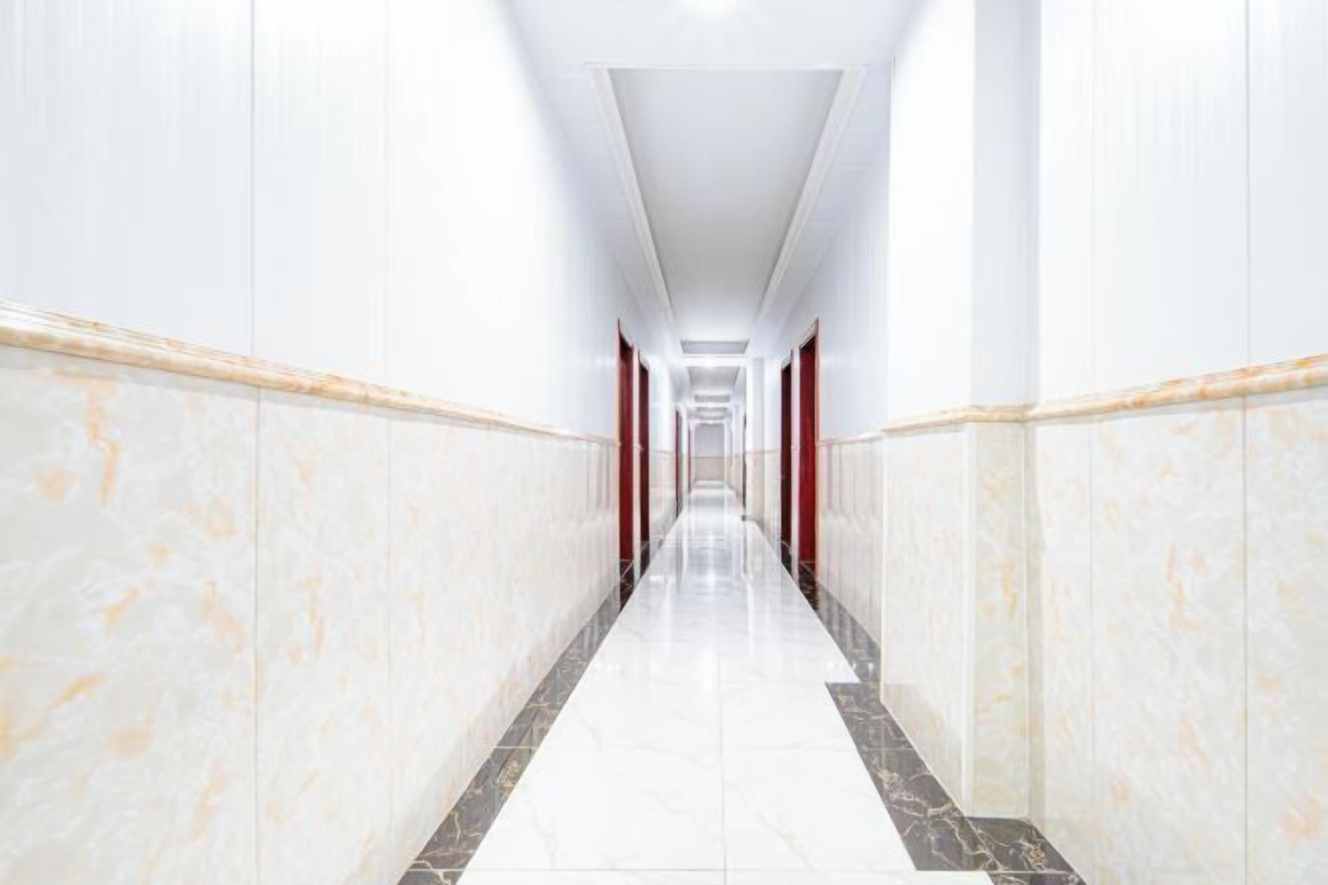A long, narrow hallway with white marble walls and a marble floor, leading to a distant end.
