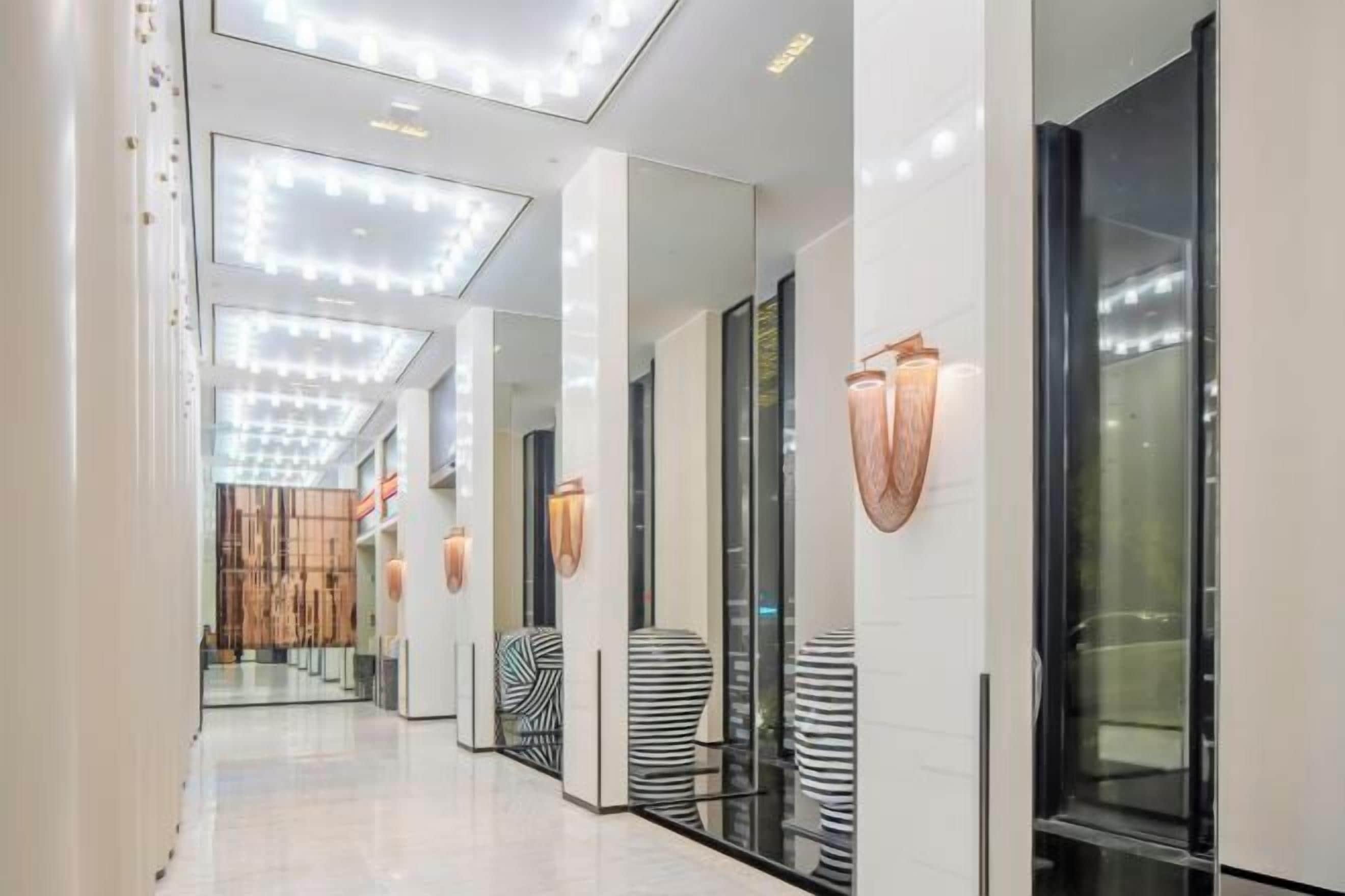 Un pasillo de hotel moderno con superficies reflectantes, puertas de vidrio e iluminación contemporánea.