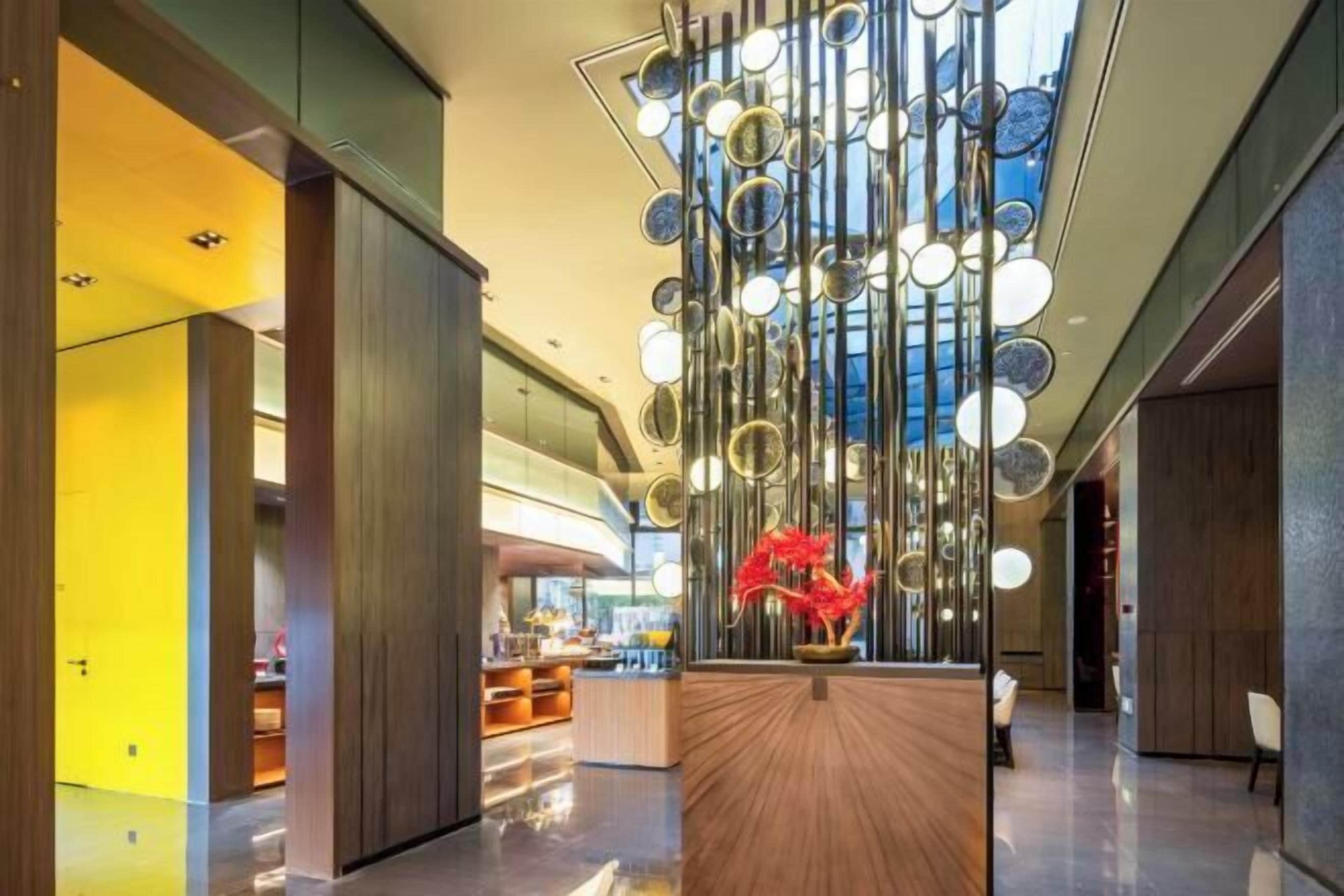 Un lobby moderno con un mostrador de recepción central, una lámpara decorativa y vistas al espacio interior.