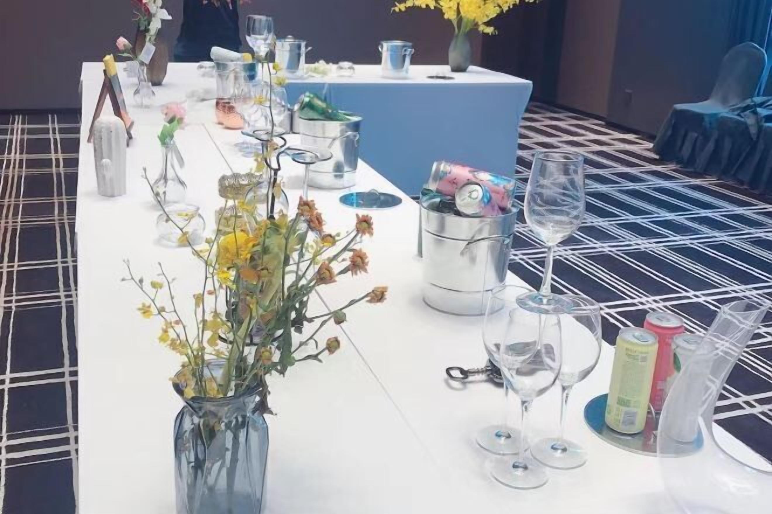 A table set with various items including a vase with flowers, wine glasses, and cans in a container.