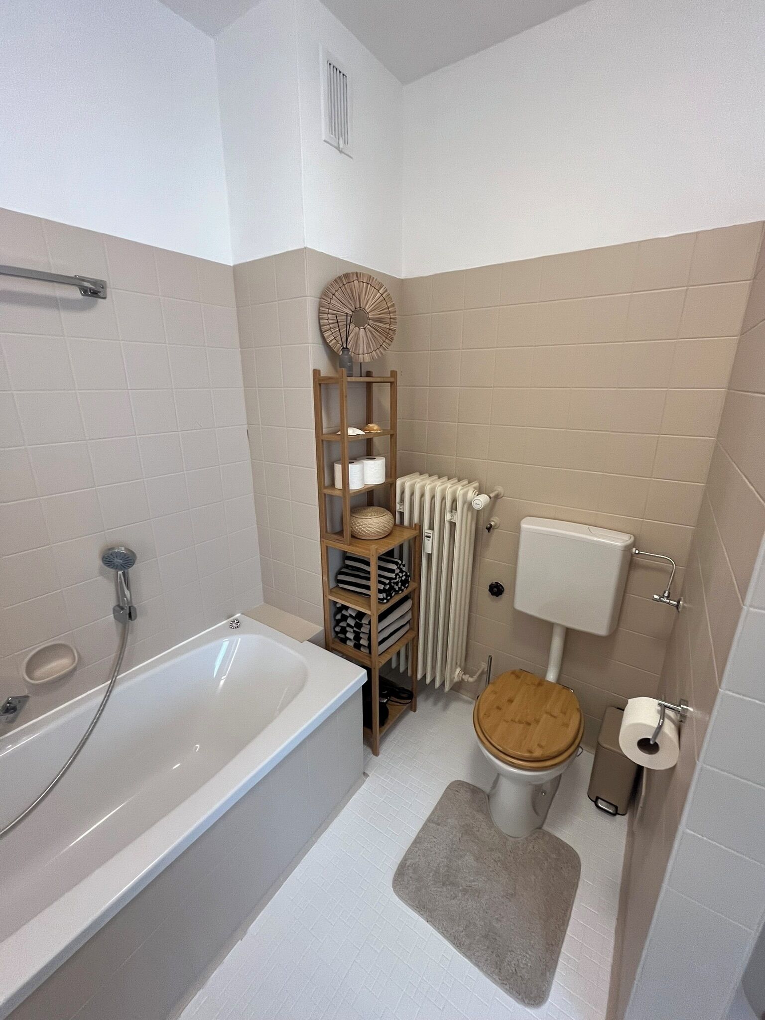 Une salle de bain équipée d’une baignoire, de toilettes et d’une étagère où sont rangées les serviettes et les articles de toilette.