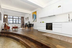 Une cuisine moderne avec des meubles blancs, un four encastré et une fenêtre donnant sur la ville.