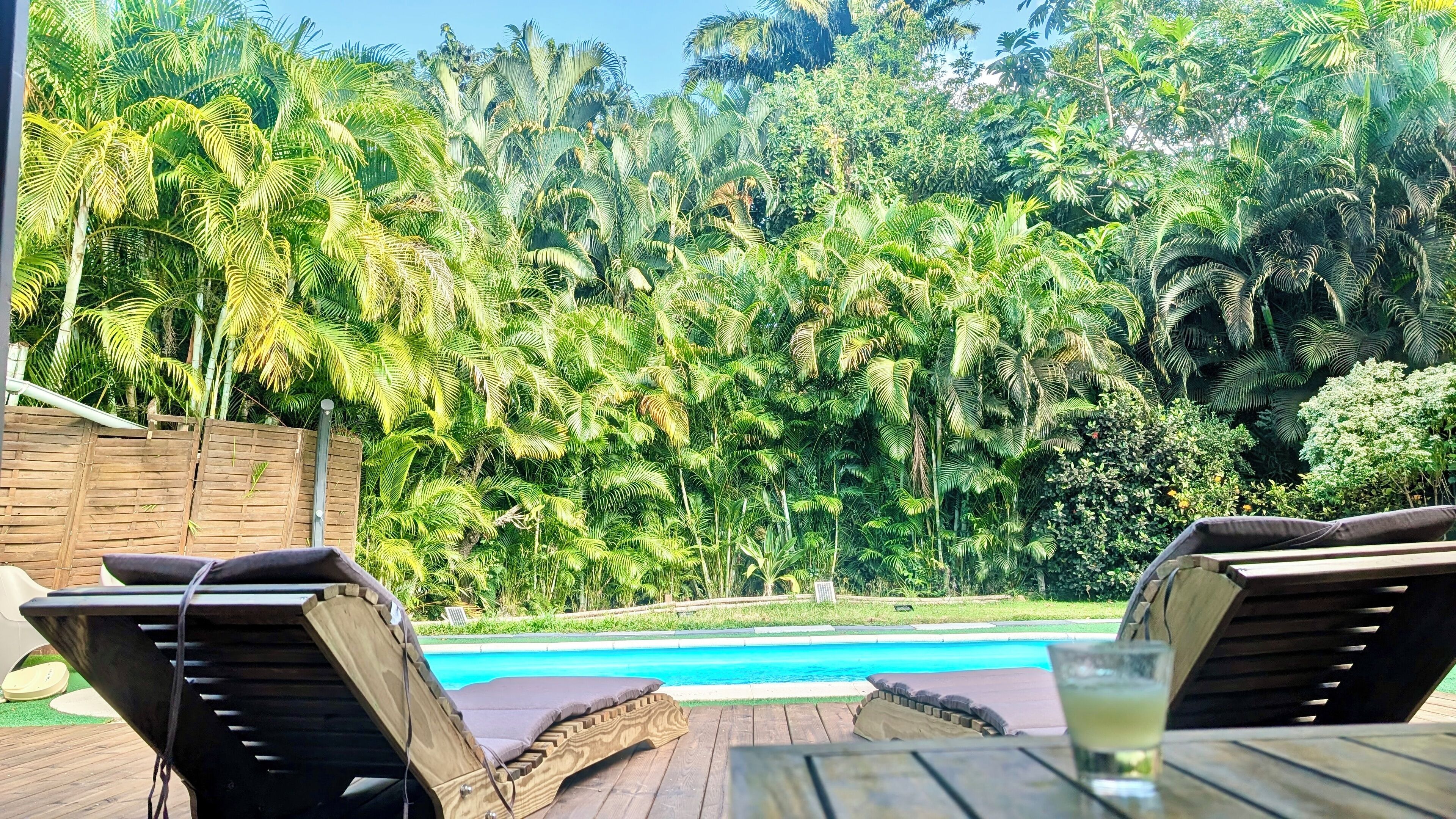 A poolside area with wooden loungers and a glass of drink.
