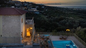 Una villa con piscina, muros de piedra y vistas al mar y colinas.