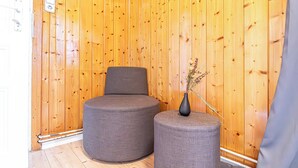 Ein Zimmer mit Holzwandverkleidung, zwei grau gepolsterten Sesseln und einem kleinen Tisch mit einer Vase.