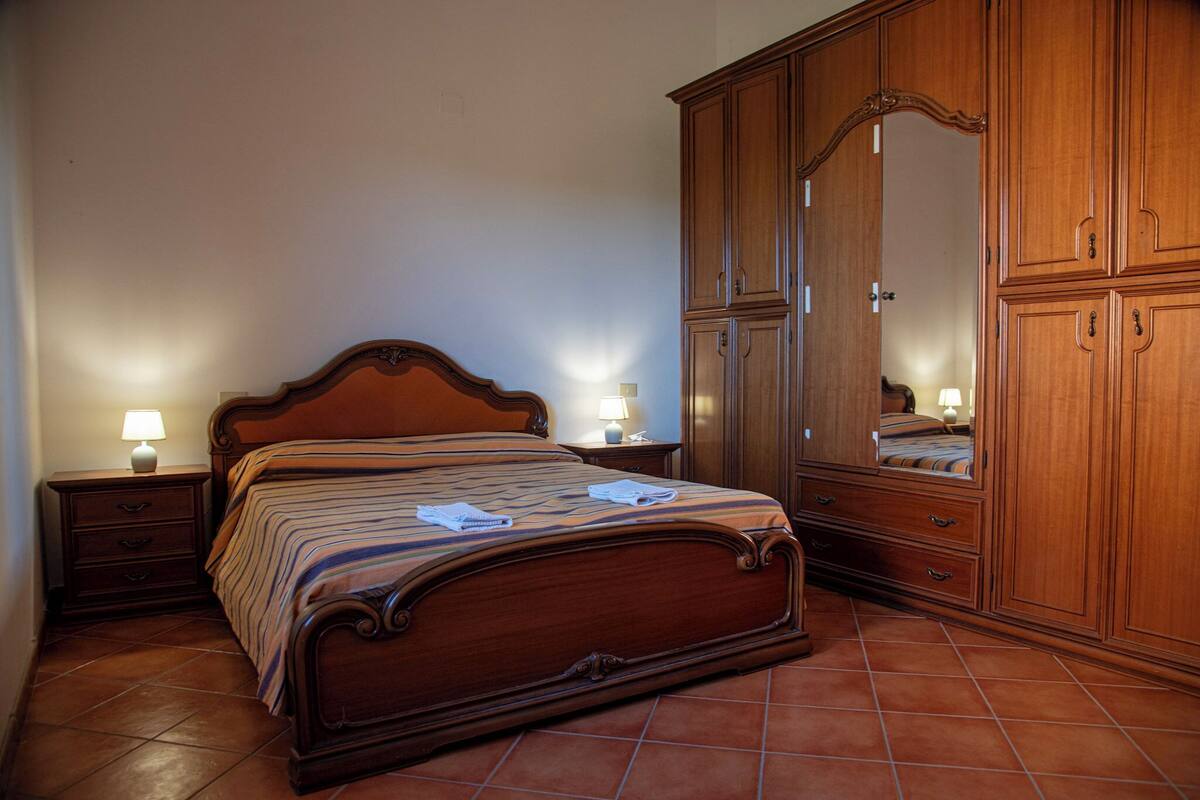 Une chambre à coucher avec un lit en bois, deux tables de chevet avec des lampes et une grande armoire.