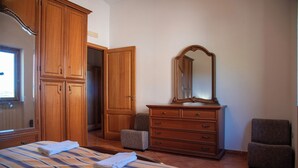 A bedroom with a large bed, wooden wardrobe, a dresser, a mirror, and two armchairs.