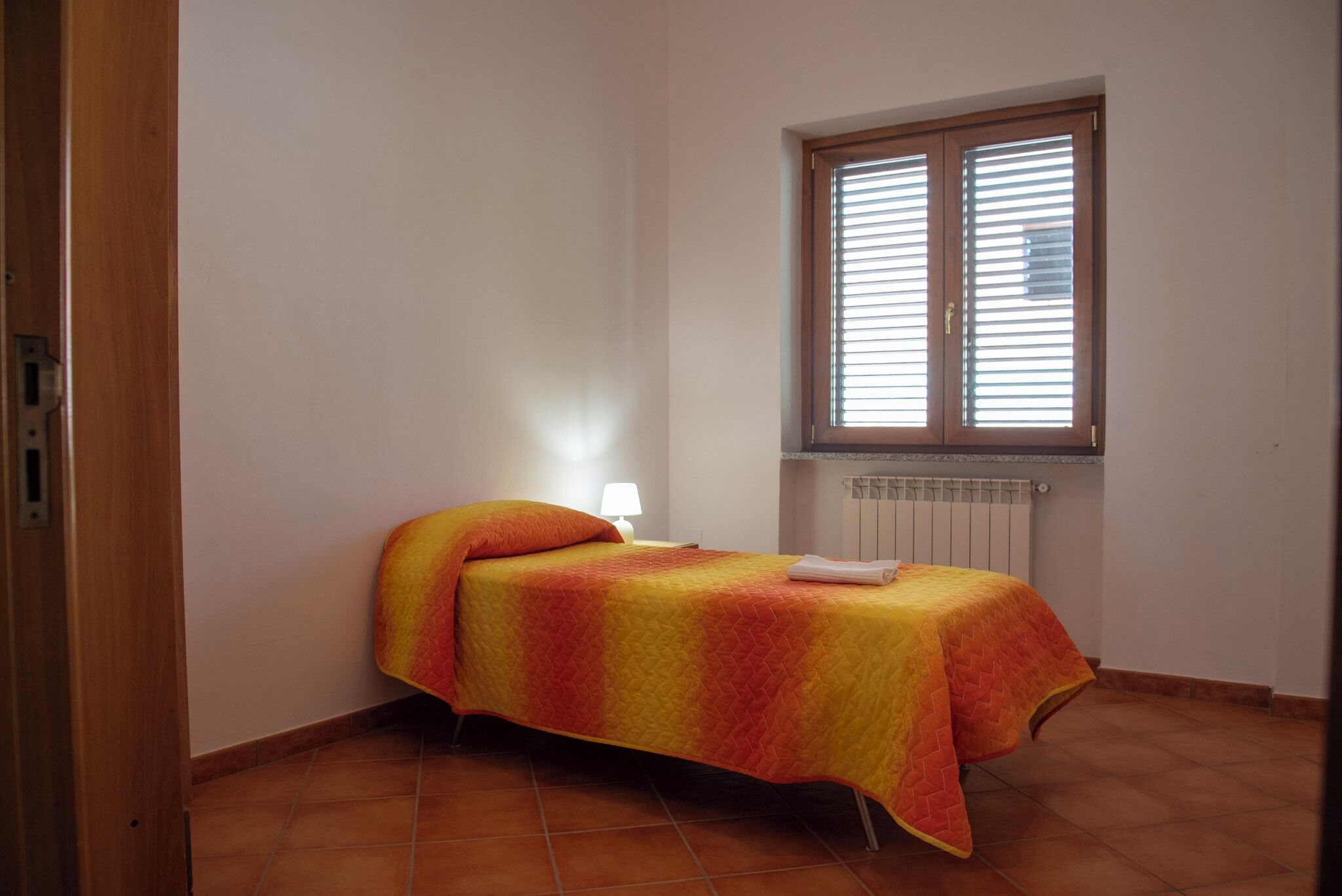 Una habitación pequeña con cama individual, ventana, radiador y lámpara de noche.