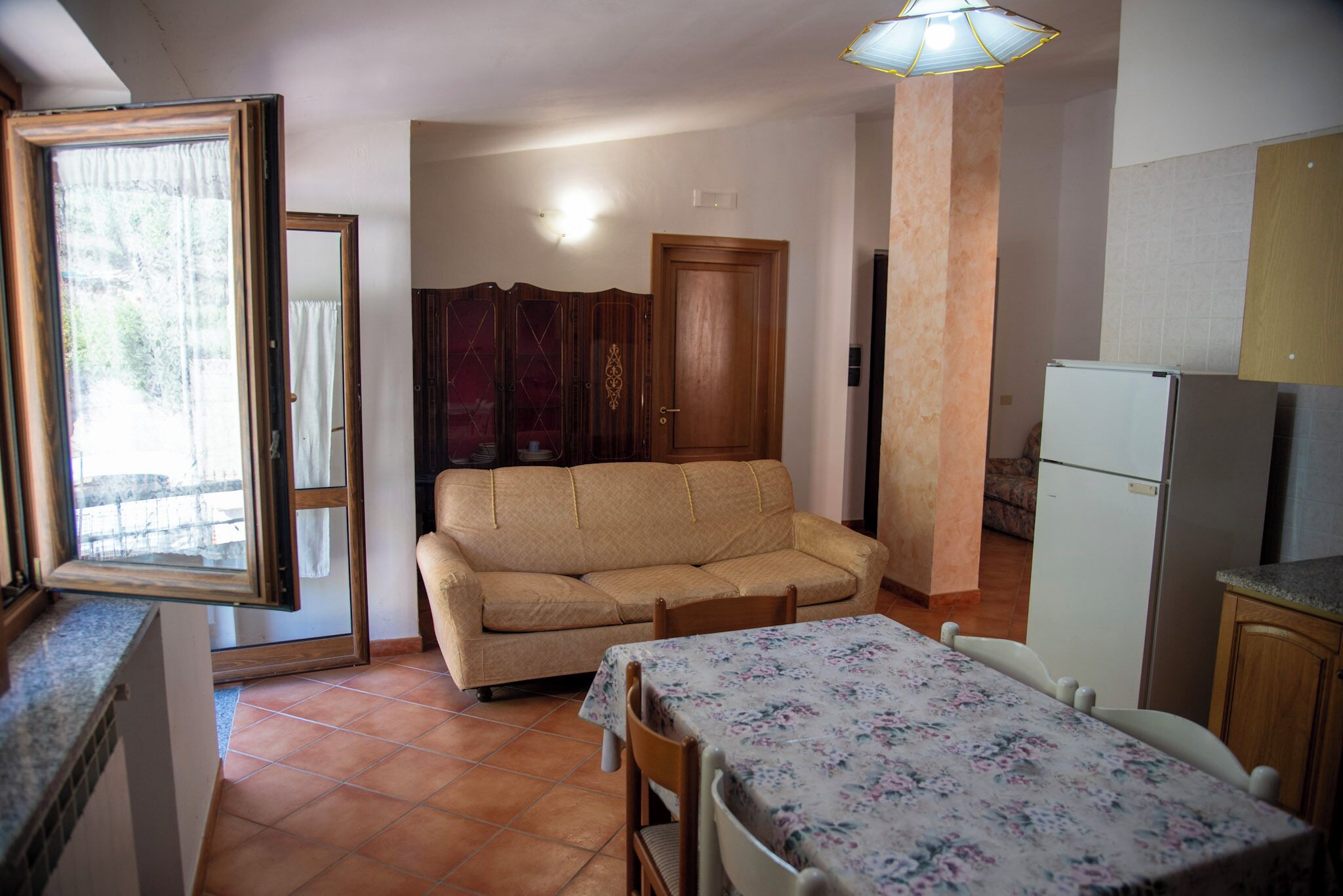 A compact living space with a sofa, a dining table, a refrigerator, and a window with curtains.