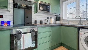 A modern kitchen with green cabinets, a microwave, a stove, and a washing machine. - CircleWay Homes - Colwick (Colwick)