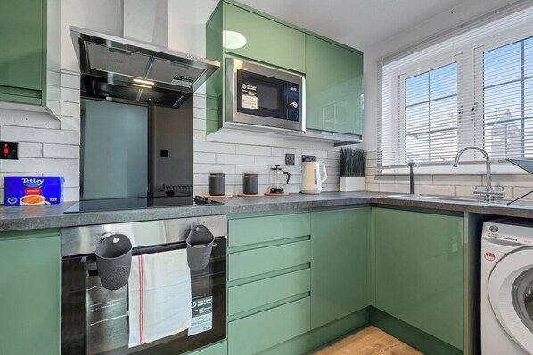 A modern kitchen with green cabinets, a microwave, a stove, and a washing machine. - CircleWay Homes - Colwick (Colwick)
