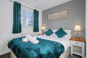 A neatly made bed with a teal blanket, two bedside lamps, and a window with curtains. - CircleWay Homes - Colwick (Colwick)