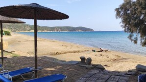 Ein Strand mit Sonnenschirmen, Liegestühlen und einer felsigen Küstenlinie.