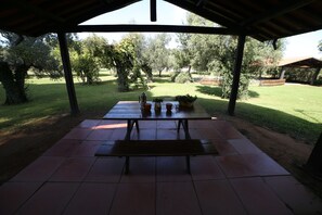 An outdoor covered patio with a picnic table and benches, surrounded by trees and a grassy lawn. - Apartment with pool in a family farmhouse on the Tuscan coast. (Castagneto Carducci)