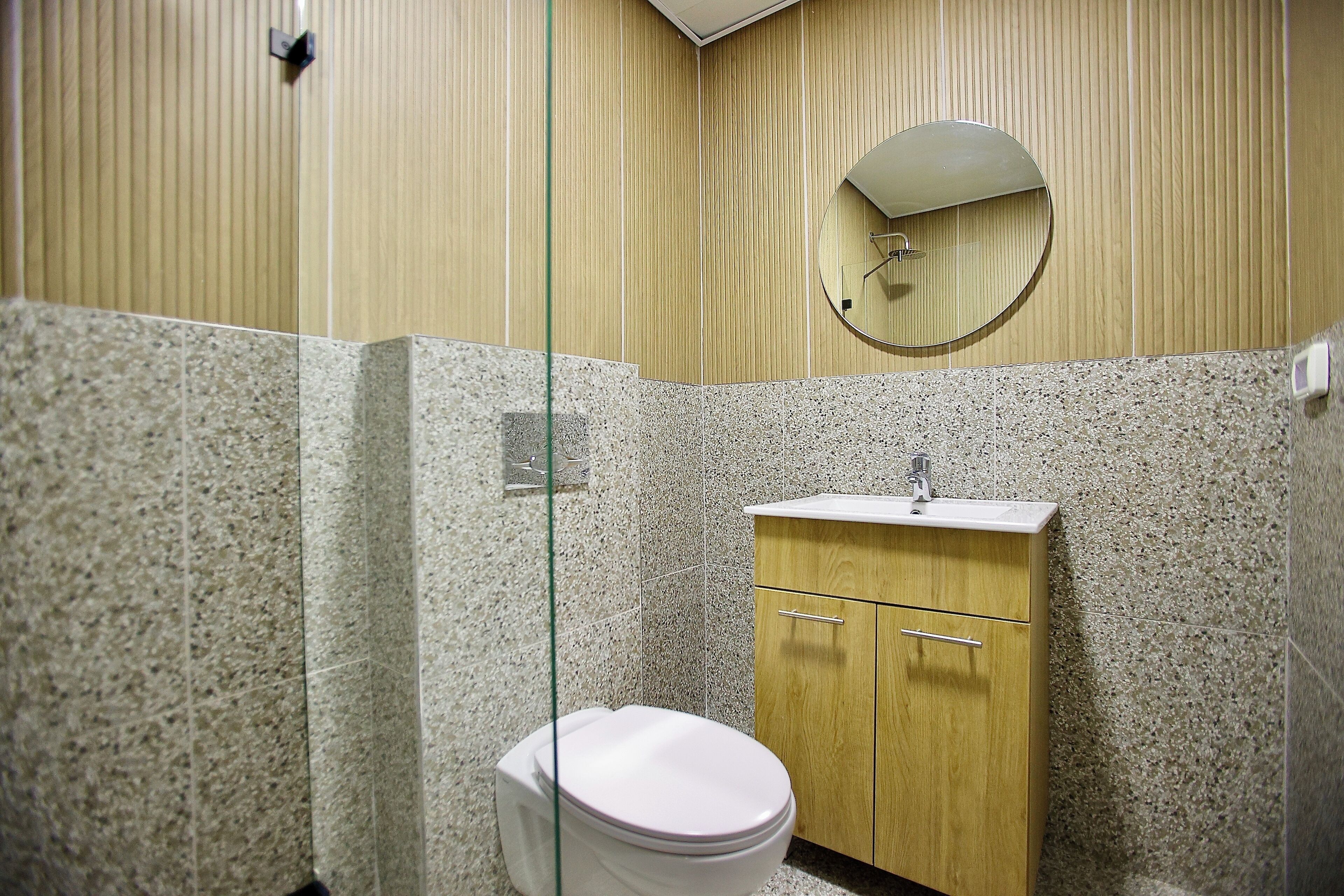 A bathroom with a toilet, a wooden cabinet with a sink, and a round mirror on the wall.