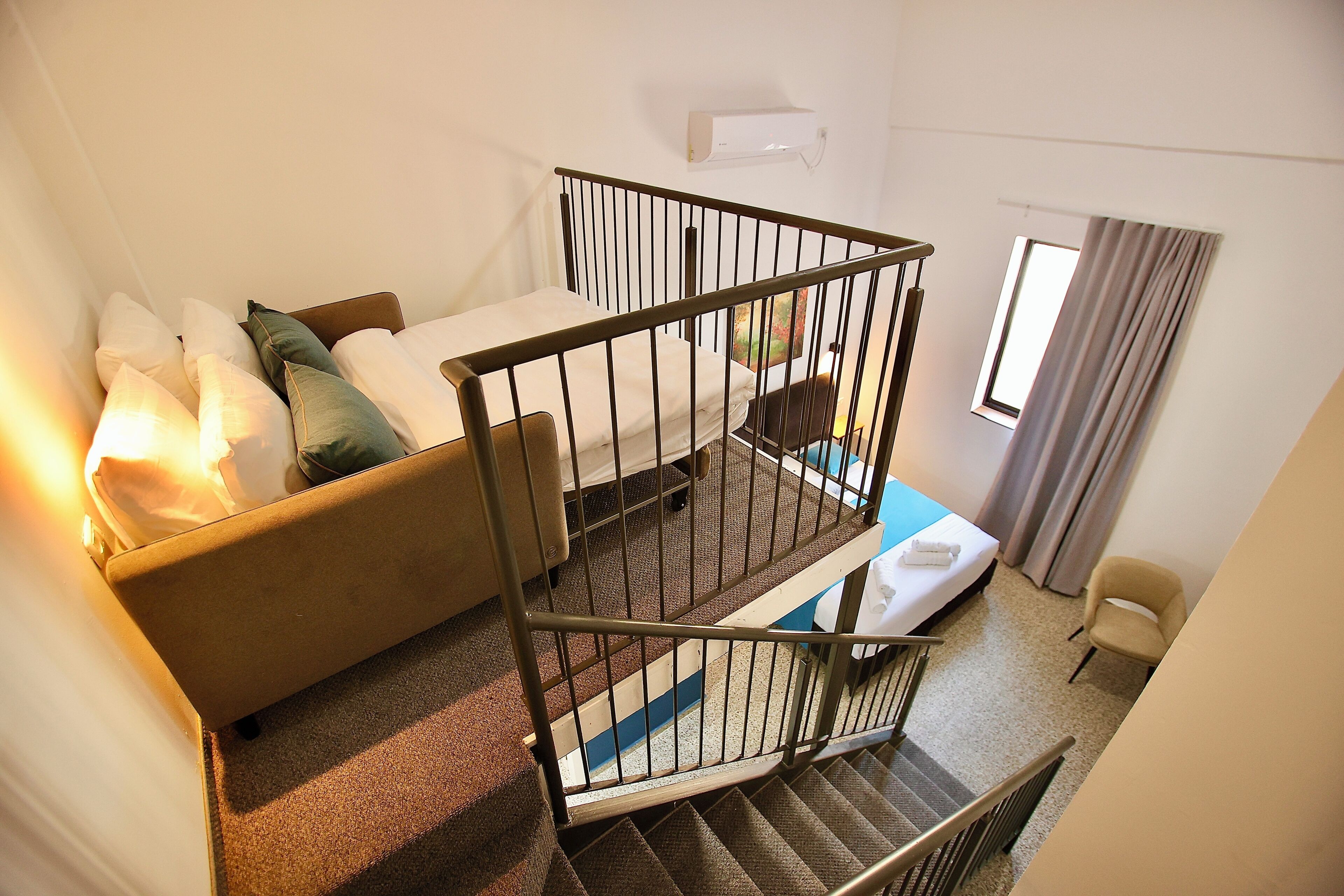 A hotel room with a bed, a sofa, a staircase, and a window with curtains.