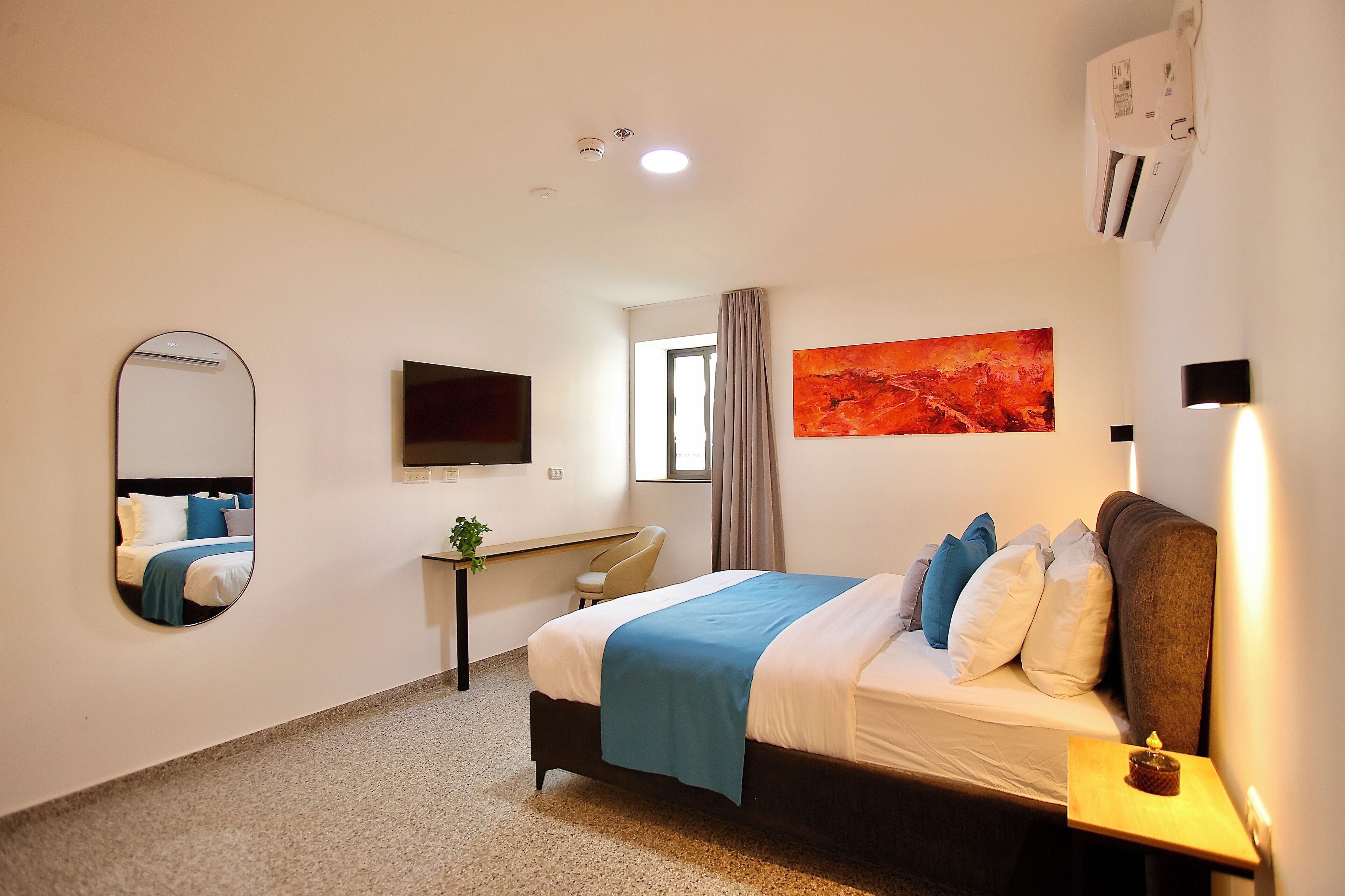 Un dormitorio con cama, escritorio, silla, televisor, un cuadro y aire acondicionado.