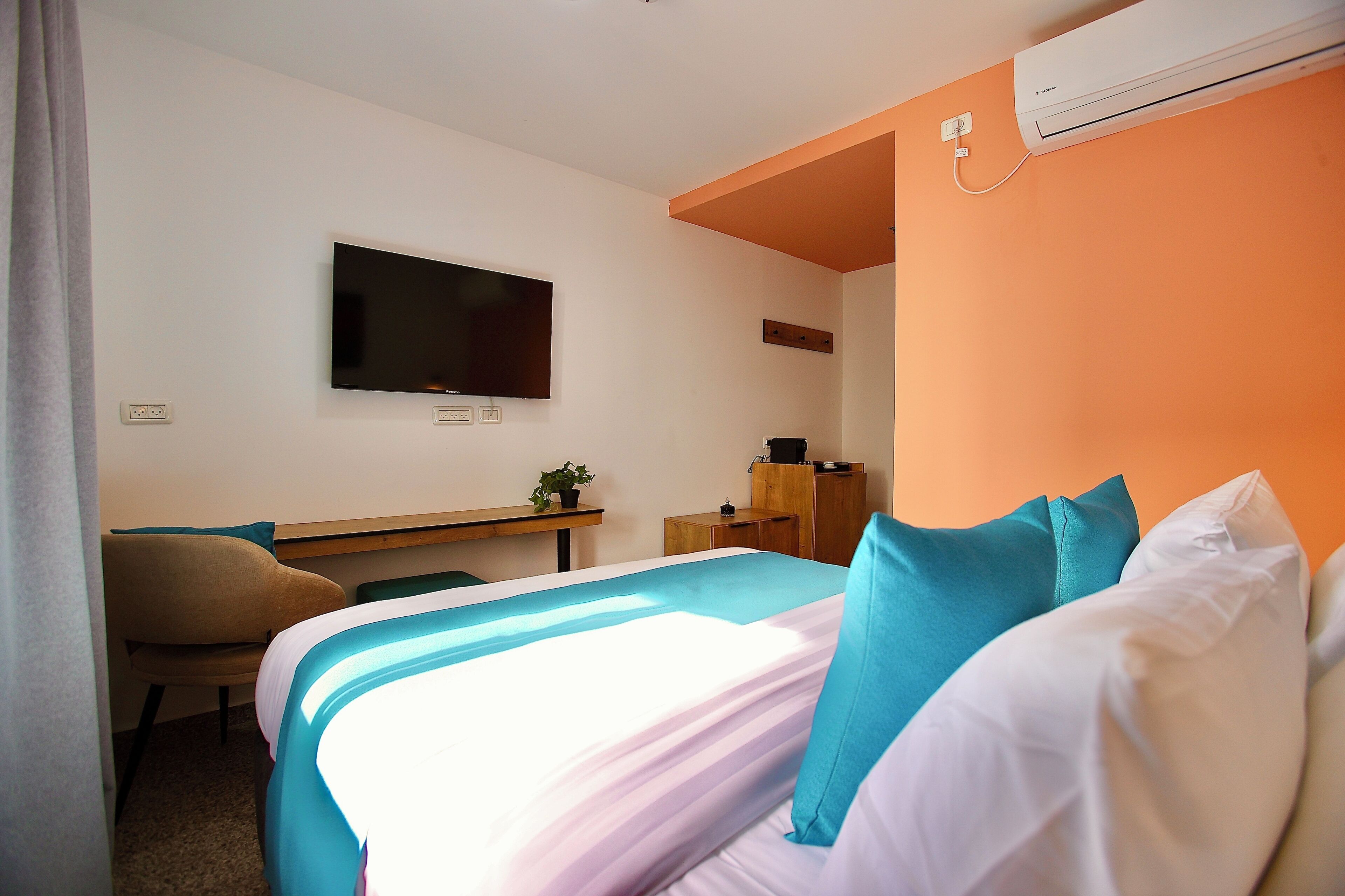 A hotel room with a bed, a desk, a chair, a television, and an air conditioning unit.