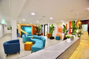 A modern lobby with a curved blue sofa, a wooden reception desk, and potted plants. - Azura Boutique Hotel (Tiberias)