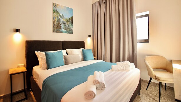 A neatly made bed with a blue and white bedspread, two pillows, and two rolled towels on the bed. - Azura Boutique Hotel (Tiberias)