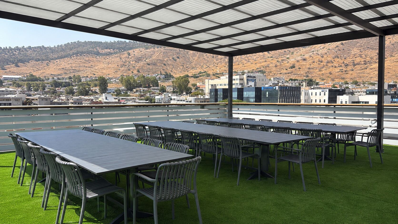 Une terrasse sur le toit, dotée de nombreuses tables et chaises, offrant une vue sur un paysage vallonné et un ciel dégagé.