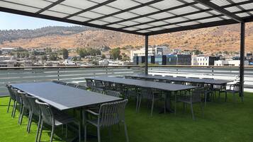 Une terrasse sur le toit, dotée de nombreuses tables et chaises, offrant une vue sur un paysage vallonné et un ciel dégagé.