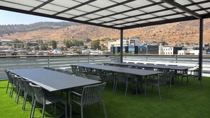 Une terrasse sur le toit, dotée de nombreuses tables et chaises, offrant une vue sur un paysage vallonné et un ciel dégagé.
