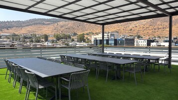 Una terraza en la azotea con varias mesas y sillas, vistas a un paisaje montañoso y cielo despejado.