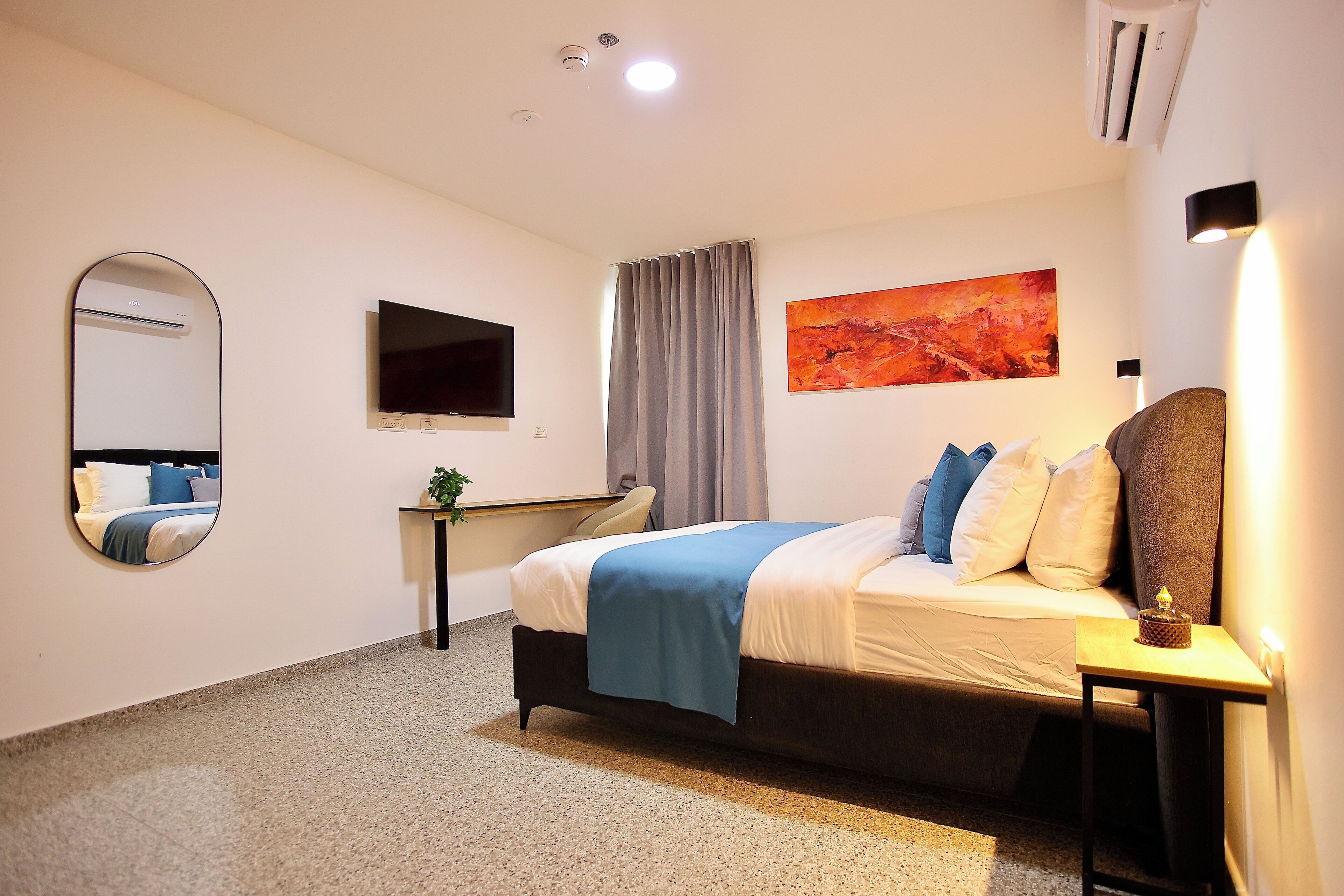 Habitación de hotel con cama, escritorio, espejo, televisión de pantalla plana y un cuadro en la pared.