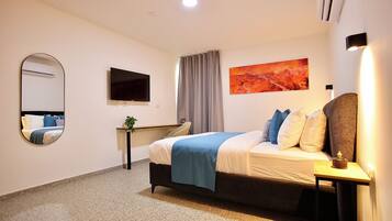 Habitación de hotel con cama, escritorio, espejo, televisión de pantalla plana y un cuadro en la pared.