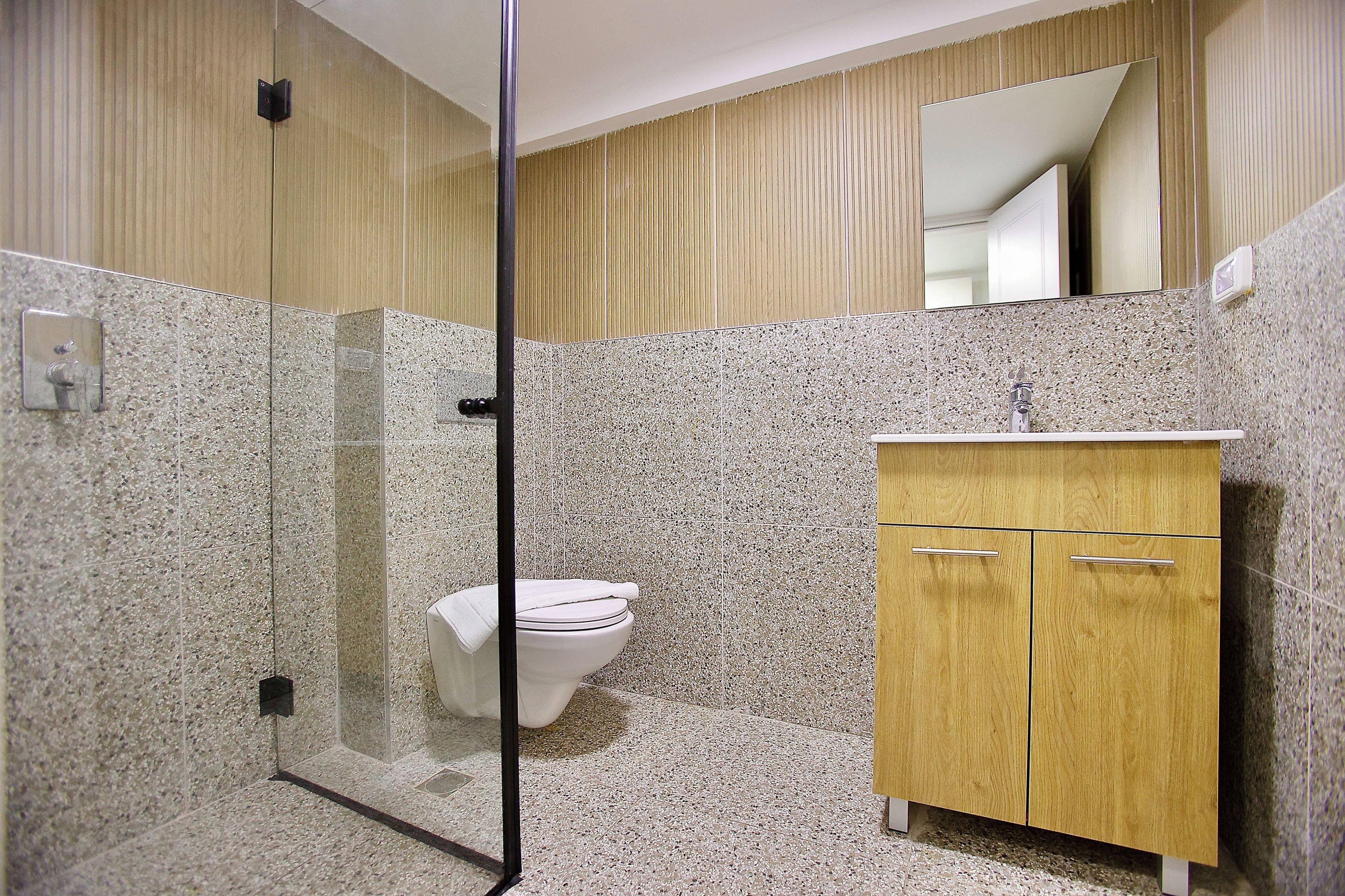 Un baño con cabina de ducha de vidrio, inodoro blanco y tocador de madera con lavamanos.