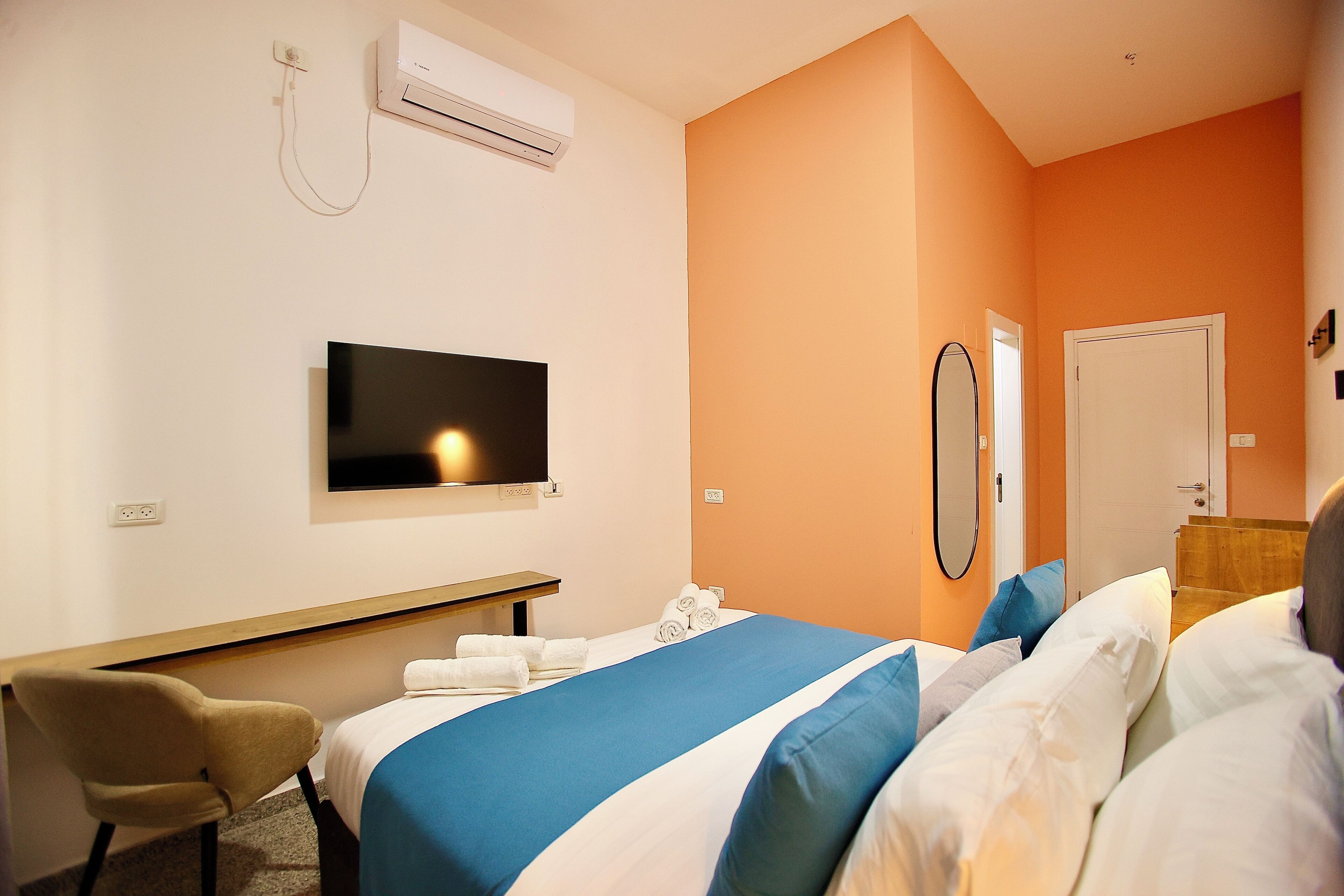 Una habitación de hotel con una cama, una silla, un televisor, aire acondicionado y una puerta.