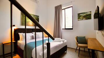 Une chambre d’hôtel comprenant un lit, un bureau, une chaise, une fenêtre avec des rideaux et des œuvres d’art accrochées aux murs.