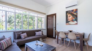 Un salon moderne comprenant un canapé, une table basse, une table à manger avec des chaises et une grande fenêtre donnant sur un paysage verdoyant.